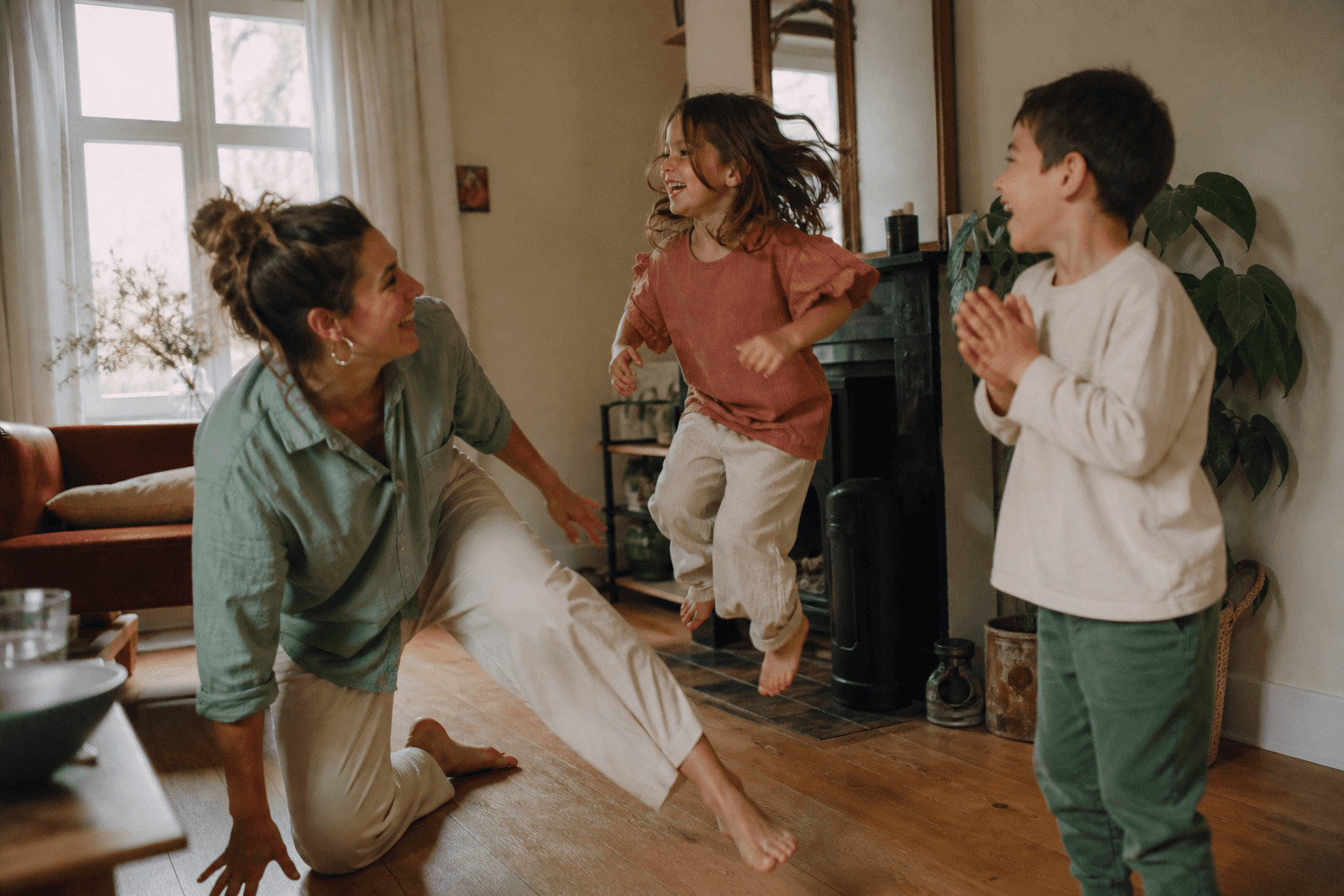 Een ouder en twee kinderen lachen en bewegen samen in de woonkamer
